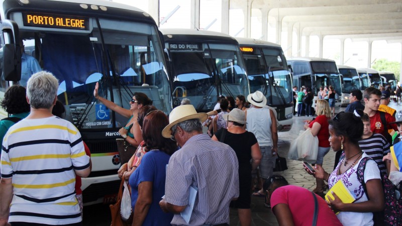 A foto mostra dezenas de pessoas circulando no setor de embarque da rodoviária de Porto Alegre, com cerca de dez ônibus estacionados nos boxes.