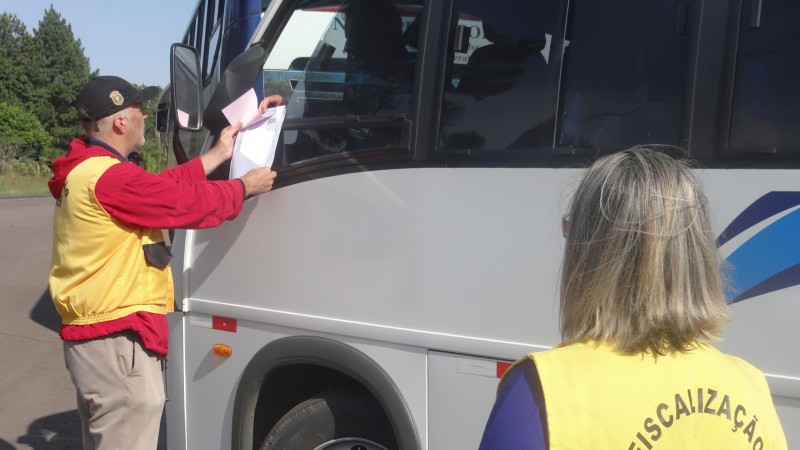 Na foto, dois fiscais com coletes amarelos do Daer verificam a documentação de um micro-ônibus de turismo.