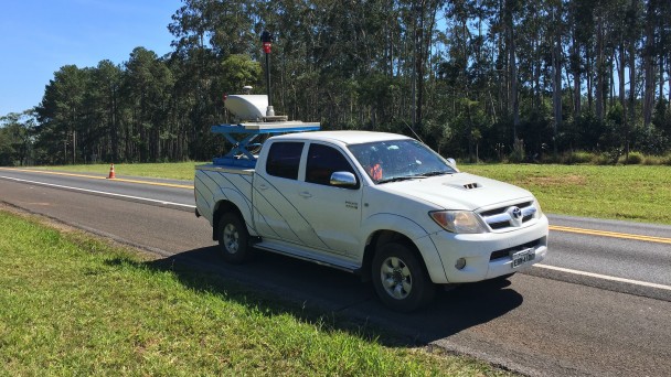 Na foto, uma caminhonete branca transita por uma estrada pavimentada com uma câmera 360 graus instalada na sua caçamba.