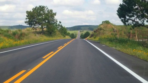 A foto mostra a RSC-453, na Serra, com asfalto em boas condições e sinalização da pista renovada. Às margens da estrada, árvores e arbustos. Ao fundo, vales.
