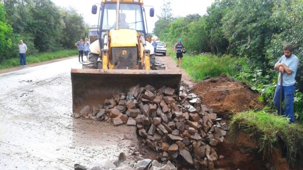 Na foto, uma patrola empurra pedras para o buraco da ERS-401 aberto pelo temporal. Um funcionário com uma pá olha o trabalho. Há mais pessoas ao fundo.
