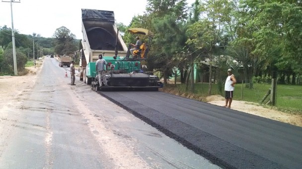 Na foto, uma máquina despeja material asfáltico no trecho em obras da ERS-713, em Sertão Santana. Funcionários acompanham o trabalho.