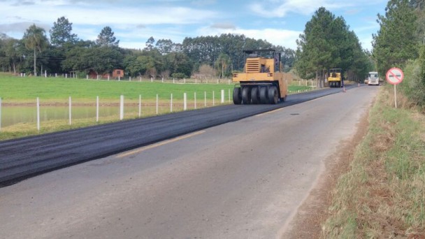 A foto mostra duas máquinas com rolo compressor passando sobre um trecho com material asfáltico recém colocado na ERS-400. A outra faixa da rodovia ainda não recebeu a nova camada.