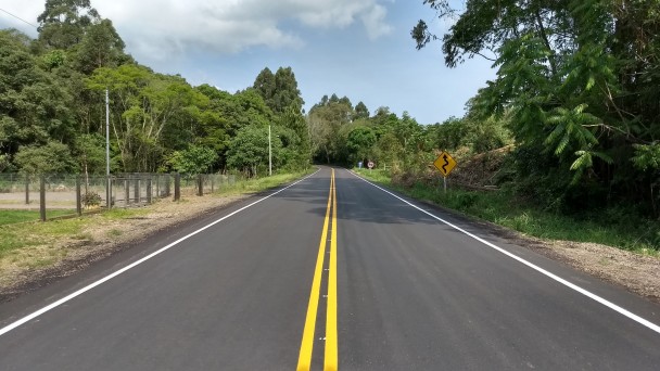 A foto mostra um trecho da ERS-400 em reta, com o asfalto renovado e a pintura dos eixos laterais e central revitalizada. Há placas de sinalização às margens, assim como árvores.