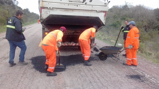 A foto mostra a imagem de três funcionários tapando buracos da rodovia. Um deles segura um carrinho de mão.