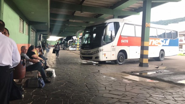 A foto mostra a rodoviária de Osório. Nela, está estacionado um ônibus da empresa UneSul e pessoas estão sentadas aguardando.