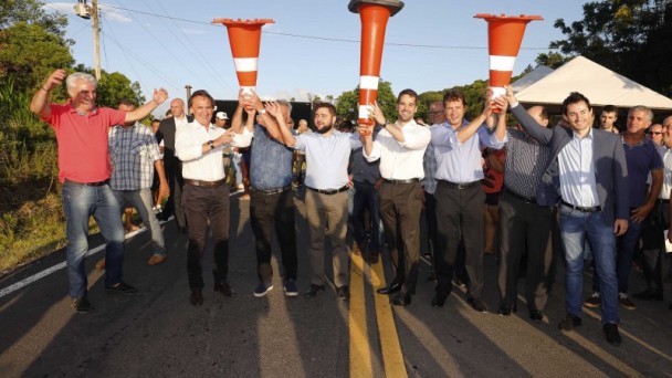 A foto mostra autoridades políticas, como o governador do estado, levantando cones para marcar a inauguração do acesso asfáltico. 