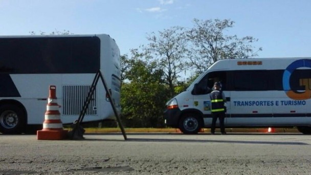 A foto mostra um veículo de fretamento e turismo sendo abordado por um fiscal do DAER.