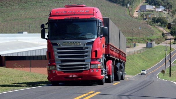A foto mostra um caminhão vermelho transitando em uma rodovia