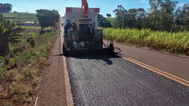 A foto mostra uma máquina nivelando o pavimento da rodovia. Em cima dela, um homem uniformizado.