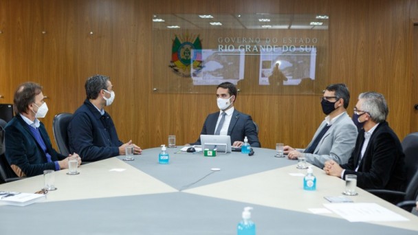 A foto mostra uma sema de reuniões. Ao centro, está sentado o governador Eduardo Leite. Ao redor, outras quatro autoridades.