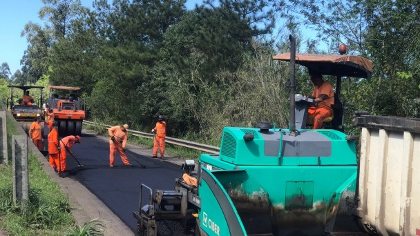 A imagem mostra homens e máquinas trabalhando na compactação do novo asfalto 