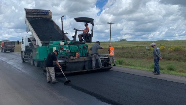 A imagem mostra máquinas e homens realizando a compactação do novo asfalto