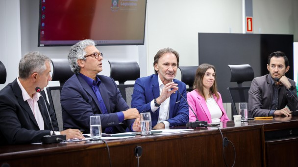 A foto mostra o secretário Costella e o diretor-geral do Daer, Luciano Faustino, em uma mesa com autoridades.