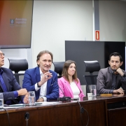 A foto mostra o secretário Costella e o diretor-geral do Daer, Luciano Faustino, em uma mesa com autoridades.