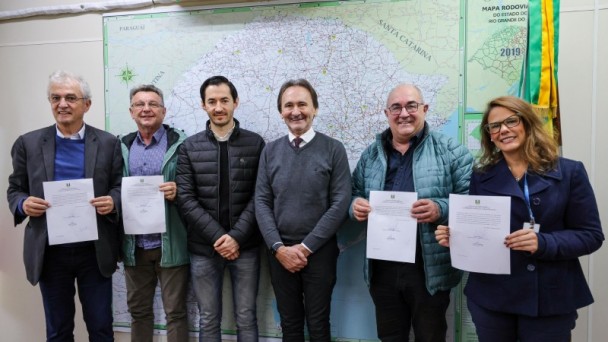 Imagem com seis pessoas em frente a mapa do Rio Grande do Sul.